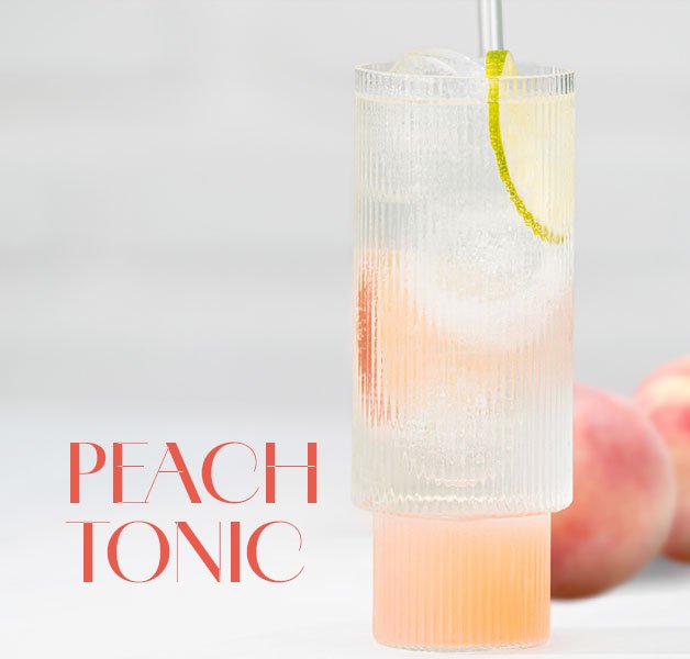 Hohes Glas mit hellrosa Peach Tonic Cocktail, garniert mit einer Limettenscheibe und Eiswürfeln.