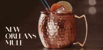 Ein glänzender Kupferbecher mit einem Cocktail, dekoriert mit Limettenscheiben und einer Orangenscheibe, auf einer dunklen Oberfläche.