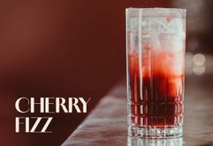 Ein Cocktailglas mit Cherry Fizz, gefüllt mit Eiswürfeln und einer leuchtend roten Flüssigkeit, strahlt Frische und Genuss aus.