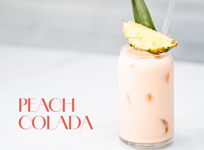 Glas mit rosa Peach Colada Cocktail, garniert mit einer Ananasscheibe und einem Ananasblatt.