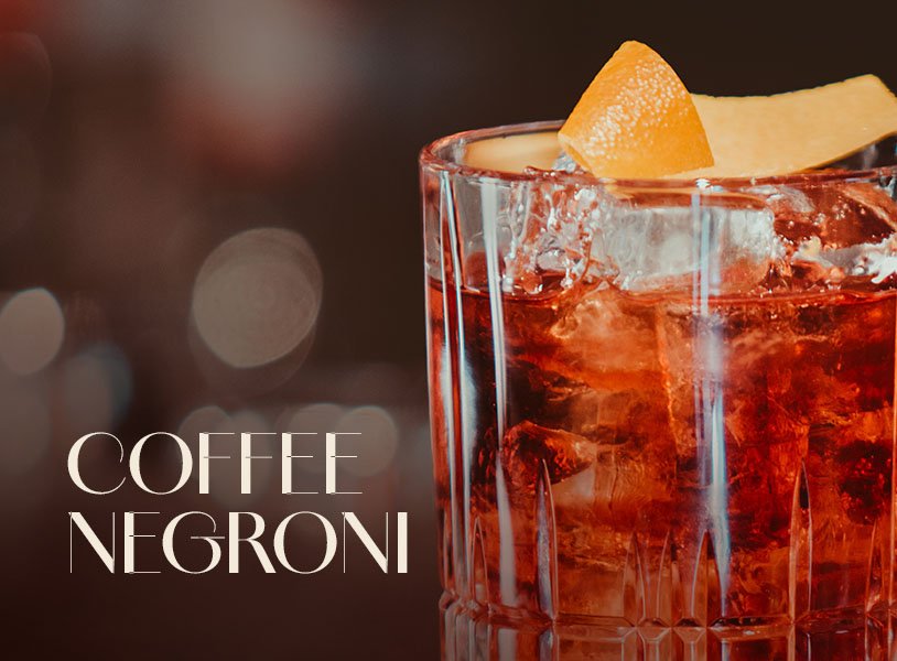 Tumbler-Glas mit rotem ECKES Coffee Negroni Cocktail, garniert mit einer Orangenzeste und Eiswürfeln.