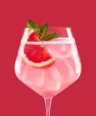 Ein elegantes Glas mit einem erfrischenden Cocktail, gefüllt mit Eis und garniert mit frischen Minzblättern und Grapefruitscheiben.