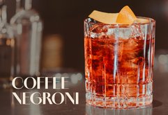 Ein elegantes Glas mit einem Coffee Negroni, gefüllt mit Eis und einer Orangenscheibe, auf einer stilvollen Bar.