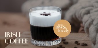 Ein Glas Irish Coffee mit einer cremigen Schicht Sahne und Kaffeebohnen auf der Oberfläche, auf einem Holztisch platziert.