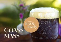 Im Vordergrund steht ein Glas mit schaumigem, dunklem Bier, während im Hintergrund sanfte, grüne Farben und Blumen sichtbar sind.