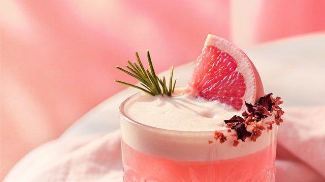 Ein erfrischender Cocktail in einem Glas, garniert mit einer Grapefruit-Scheibe und einem Zweig Rosmarin.