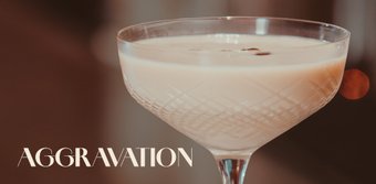Ein elegantes Cocktailglas mit einer cremigen, hellen Flüssigkeit und einer Kaffeebohne als Garnitur steht im Fokus.