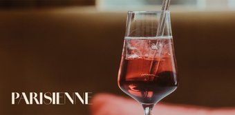 Ein elegantes Glas mit einem roten Getränk, gefüllt mit Eiswürfeln, steht auf einem Tisch in einem stilvollen Ambiente.