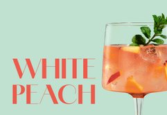 Ein erfrischender Cocktail in einem eleganten Glas, gefüllt mit Pfirsichstücken und einem Minzblatt als Garnitur.
