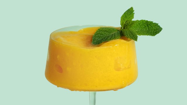 Ein köstlicher, fruchtiger Drink in einem Glas, leuchtend gelb und mit einem Minzblatt dekoriert, strahlt Sommerfrische aus.