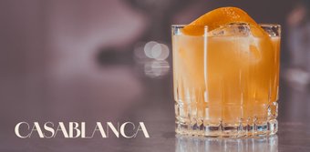 Ein elegantes Glas mit einem orangefarbenen Cocktail, garniert mit einer Orangenscheibe, auf einem stilvollen Tisch.
