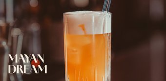 Ein erfrischendes Getränk in einem hohen Glas, gefüllt mit orangefarbener Flüssigkeit und Eiswürfeln, steht auf einer Bar.