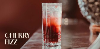 Ein Cocktailglas mit Cherry Fizz, gefüllt mit Eiswürfeln und einer leuchtend roten Flüssigkeit, strahlt Frische und Genuss aus.