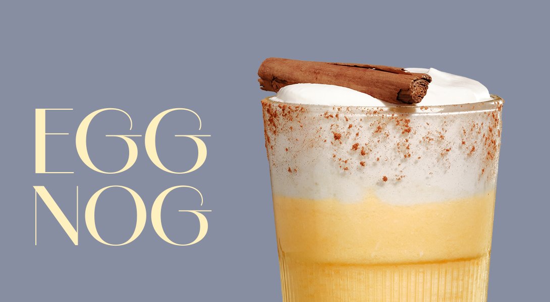 Glas mit gelbem Eggnog Cocktail, mit einer Schaumkrone, Zimtstange und Muskatnuss bestreut.