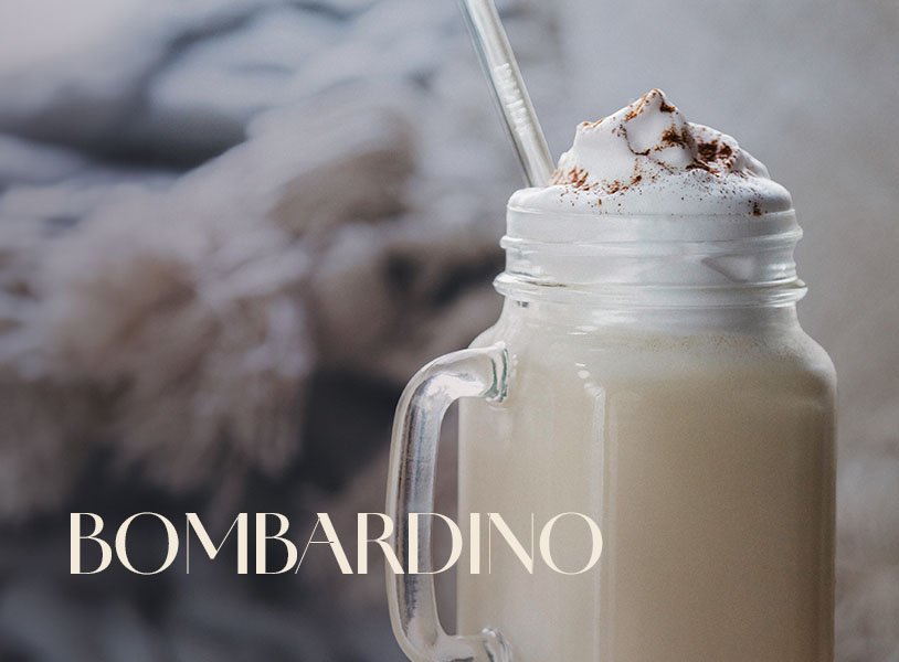 Glas mit ECKES Bombardino, garniert mit Sahne und Schokoladenstreuseln, vor einem gemütlichen Hintergrund