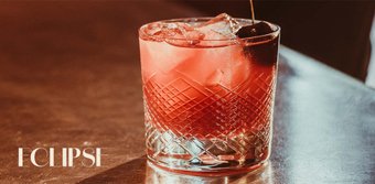 Der Cocktail im Glas hat eine leuchtend rote Farbe und wird von Eiswürfeln und einer Kirsche begleitet, ideal für einen Abend.