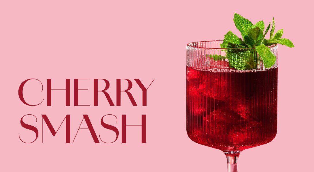 Glas mit ECKES Cherry Smash Cocktail auf Eis, garniert mit frischer Minze, vor einem rosafarbenen Hintergrund