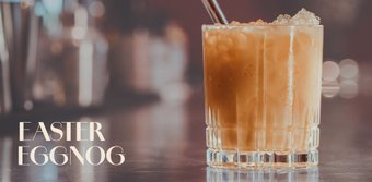 Ein erfrischendes Getränk aus Eierlikör mit Eiswürfeln, das in einem stilvollen Glas präsentiert wird, umgeben von verschwommenen Flaschen.