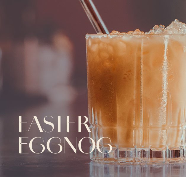 Glas mit ECKES Egg Nog Cocktail auf Eis, mit einem Strohhalm, vor einem unscharfen Barhintergrund