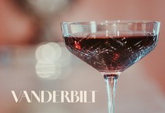 Das Glas, gefüllt mit einem rubinroten Getränk, hebt sich vor einem sanften, verschwommenen Hintergrund ab.