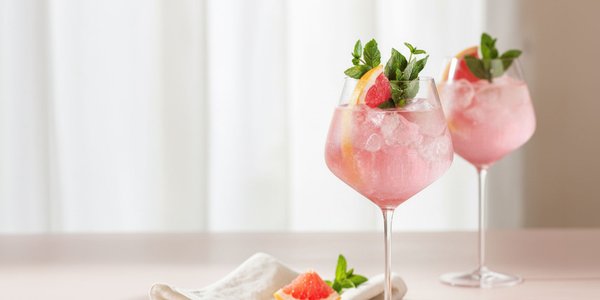 Zwei elegante Gläser mit pinkem Getränk, garniert mit Minze und Grapefruitscheiben, stehen auf einem hellen Tisch.