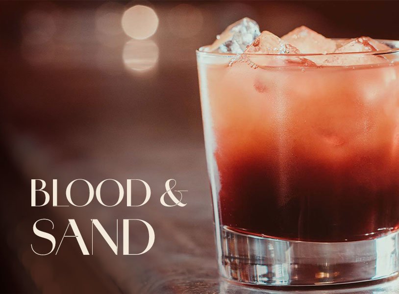 Glas mit ECKES Blood & Sand Cocktail auf Eis, vor einem unscharfen, dunklen Hintergrund mit der Aufschrift "Blood & Sand".