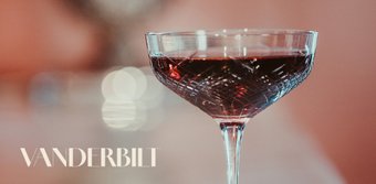 Das Glas, gefüllt mit einem rubinroten Getränk, hebt sich vor einem sanften, verschwommenen Hintergrund ab.