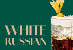 Ein eleganter White Russian Cocktail in einem Glas mit Eis, garniert mit Sahne und einer gelben Frucht.
