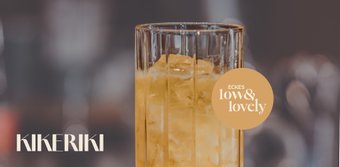 Ein elegantes Glas mit einem gelben Getränk und Eiswürfeln, das in einem modernen, verschwommenen Raum präsentiert wird.