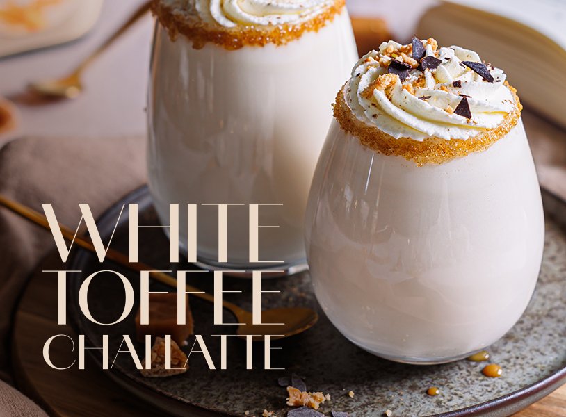 Ein köstlicher White Toffee Chai Latte, serviert in einem Glas mit Sahnehaube und Schokoladenstückchen, auf einem rustikalen Untergrund.