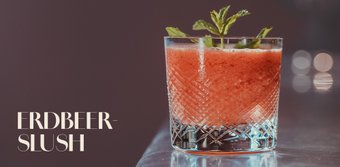 Ein erfrischender Erdbeer-Slush in einem eleganten Glas, garniert mit frischer Minze, auf einem glänzenden Tisch.