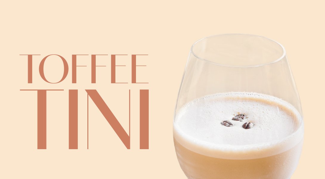 Ein elegantes Glas mit einem cremigen Toffee-Cocktail, garniert mit Kaffeebohnen, vor einem sanften, hellen Hintergrund.