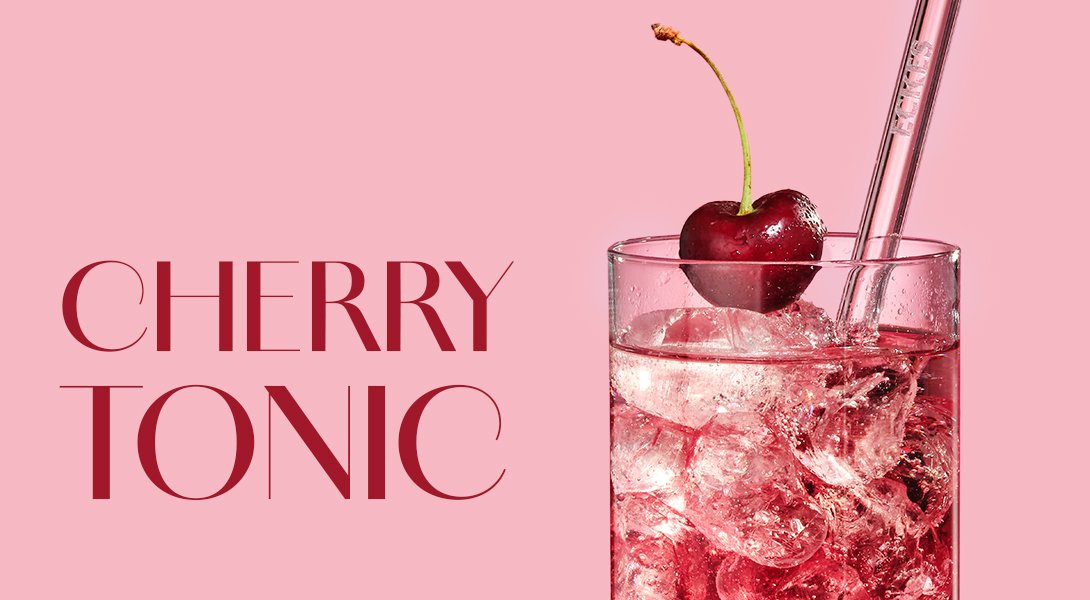 Glas mit ECKES Cherry Tonic Cocktail, garniert mit einer Kirsche und einem Strohhalm, vor einem rosafarbenen Hintergrund