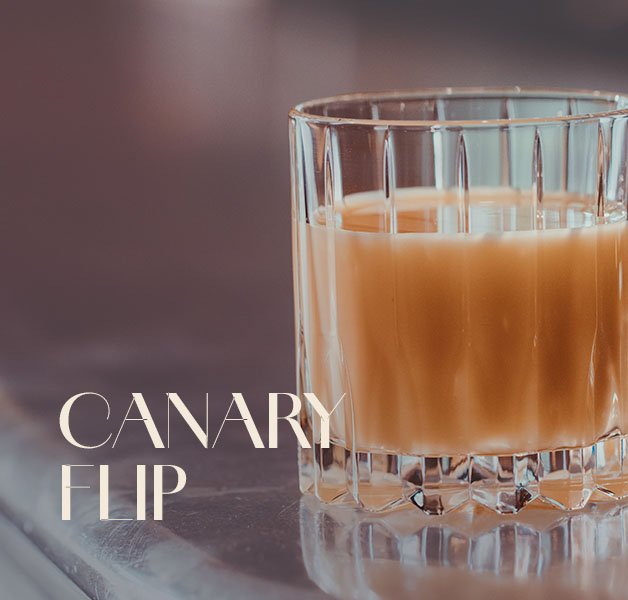 Glas mit ECKES Bombardino, garniert mit Sahne und Schokoladenstreuseln, vor einem gemütlichen Hintergrund