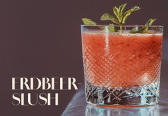 Ein erfrischender Erdbeer-Slush in einem eleganten Glas, garniert mit frischer Minze, auf einem glänzenden Tisch.