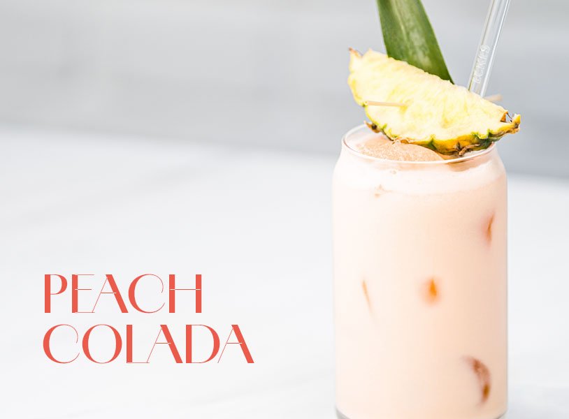 Glas mit rosa Peach Colada Cocktail, garniert mit einer Ananasscheibe und einem Ananasblatt.