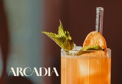 Ein Cocktail mit leuchtender orangefarbener Flüssigkeit, dekoriert mit Minze und einer Scheibe Orange auf Eis.