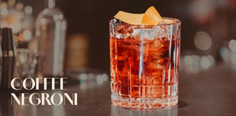 Ein elegantes Glas mit einem Coffee Negroni, gefüllt mit Eis und einer Orangenscheibe, auf einer stilvollen Bar.