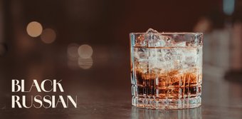 Ein Glas mit einem Black Russian Cocktail, gefüllt mit Eiswürfeln und einer dunklen Flüssigkeit, steht auf einer glänzenden Oberfläche.