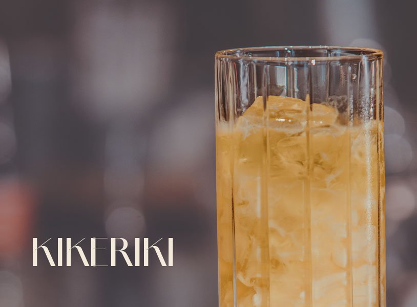 Glas mit ECKES Kikeriki Cocktail auf Eis, vor einem unscharfen Barhintergrund