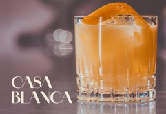 Ein elegantes Glas mit einem orangefarbenen Cocktail, garniert mit einer Orangenscheibe, auf einem stilvollen Tisch.