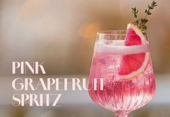 Ein stilvolles Getränk in einem klaren Glas, gefüllt mit pinkem Spritz und dekoriert mit einer Grapefruit-Scheibe.