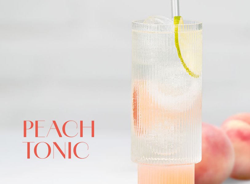 Hohes Glas mit hellrosa Peach Tonic Cocktail, garniert mit einer Limettenscheibe und Eiswürfeln.