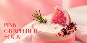 Ein erfrischender pinker Grapefruit-Cocktail, garniert mit einer Grapefruit-Scheibe und Rosmarin, vor einem sanften rosa Hintergrund.