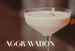 Ein elegantes Cocktailglas mit einer cremigen, hellen Flüssigkeit und einer Kaffeebohne als Garnitur steht im Fokus.