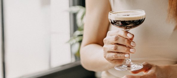 Eine Person hält zwei Gläser mit cremigen Cocktails, garniert mit Sahne, Schokoladenstückchen und Orangenschale.