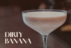Ein elegantes Cocktailglas mit einem cremigen, hellbraunen Getränk steht auf einer Bar, umgeben von verschwommenen Lichtern.