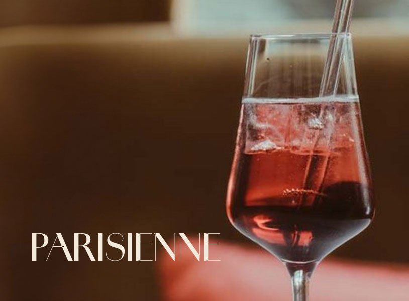 Glas mit ECKES Parisienne Cocktail, in dem ein Spritzer Flüssigkeit aufsteigt, vor einem unscharfen Hintergrund mit der Aufschrift "Parisienne".