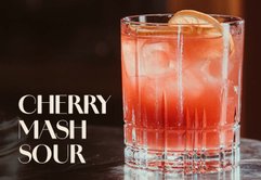 Der Cherry Mash Sour Cocktail, dekoriert mit einer Zitronenscheibe, steht auf einem eleganten Tisch aus Holz.