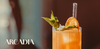 Ein Cocktail mit leuchtender orangefarbener Flüssigkeit, dekoriert mit Minze und einer Scheibe Orange auf Eis.